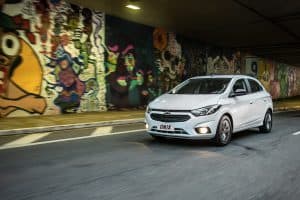 Chevrolet Onix branco em movimento, saindo de um túnel iluminado, com faróis acesos e destaque para o design urbano do hatch