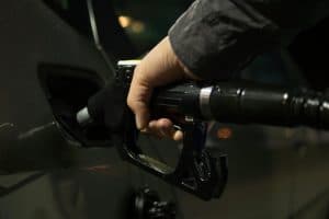 Pessoa abastecendo o carro com gasolina à noite em um posto iluminado, com destaque para a bomba de combustível.