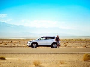 Pessoa parada em frente a um carro branco em ambiente rural, com paisagem simples ao fundo — imagem de Unsplash