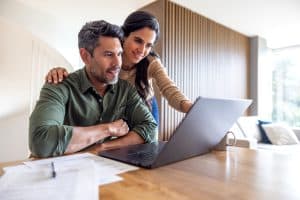 Casal olhando para o notebook enquanto organiza as finanças, planejando como juntar dinheiro para conquistar um carro seminovo.