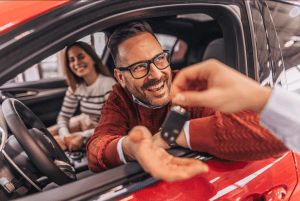 casal dentro do carro vermelho recebendo a chave, simbolizando a conquista de um seminovo.