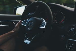 Mão no volante de carro, com foco nos botões do volante multifuncional em destaque.