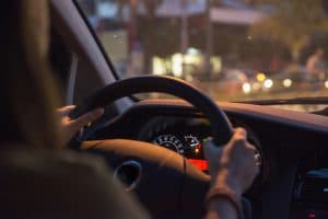 Plano fechado de duas mãos ao volante e painel do carro aceso.
