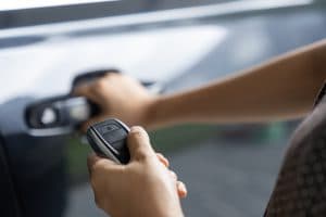 pessoa abre o carro à distância usando o dispositivo keyless, foco na mão segurando a chave eletrônica e no veículo ao fundo