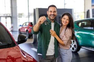 Visiting car dealership. Beautiful couple is holding a key of their new car, looking at camera and smiling