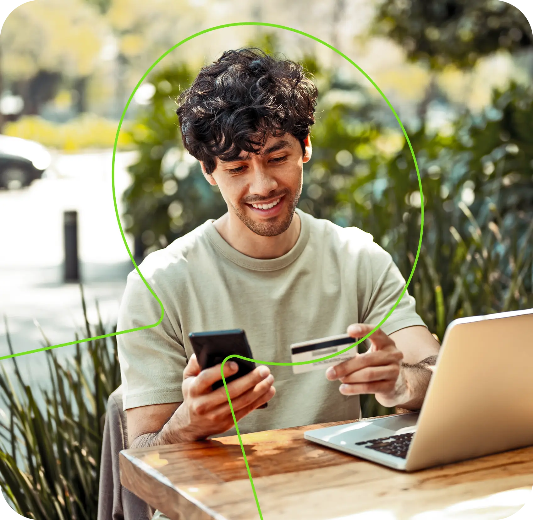 Homem sorrindo enquanto utiliza celular e cartão de crédito, com laptop sobre a mesa ao ar livre, representando facilidade no financiamento de carros seminovos na Localiza.