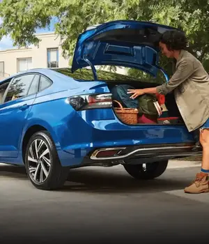 Uma mulher colocando malas no bagageiro de um carro azul.